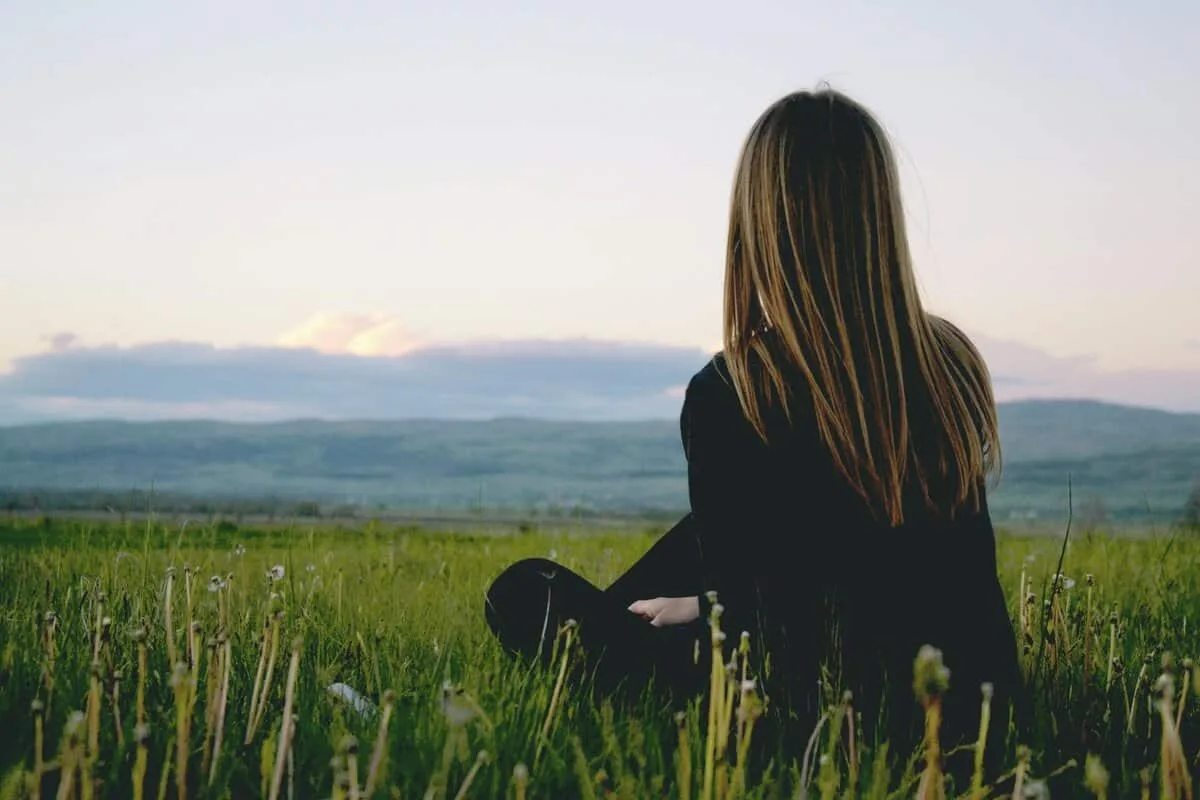 Hypnotherapy client enjoying peace in a lush green field with a scenic mountain view during sunset.