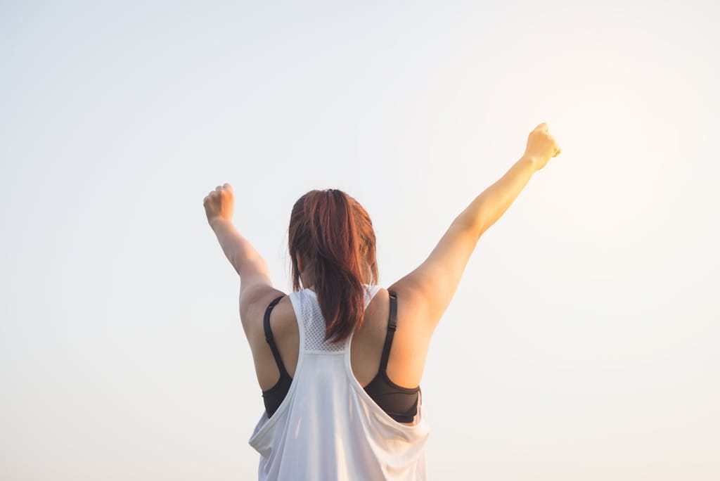 A woman celebrates success with arms raised in a bright outdoor setting - quit smoking without weight gain Melbourne hypnotherapy