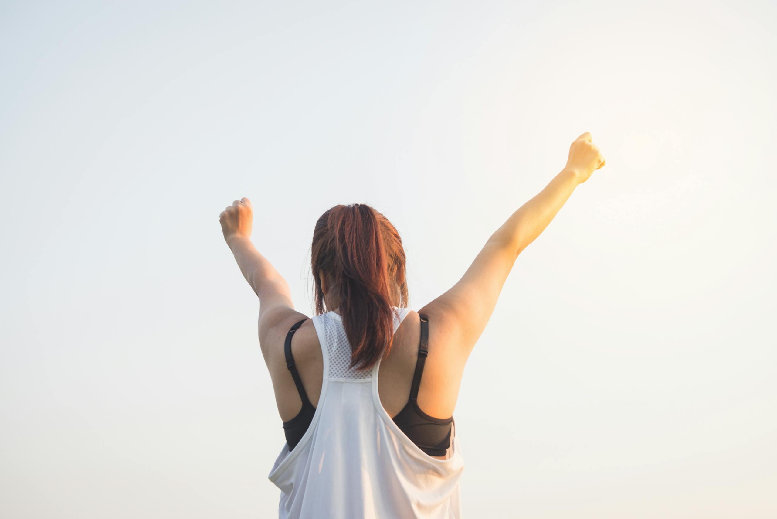 A woman celebrates success with arms raised in a bright outdoor setting - quit smoking without weight gain Melbourne hypnotherapy