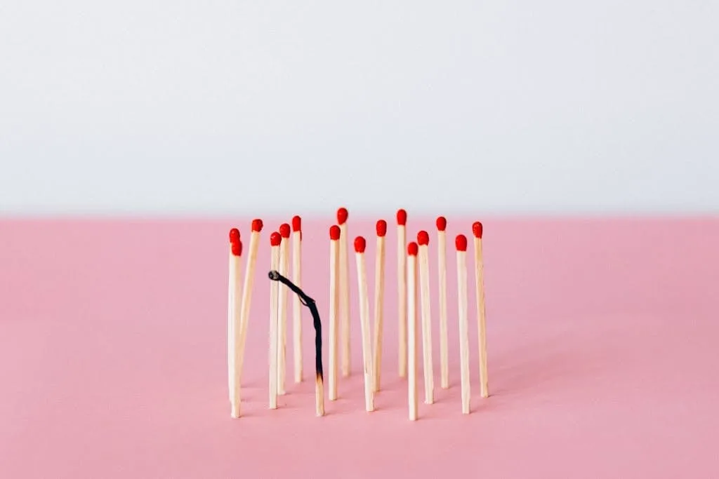 Home 1 Artistic representation of burnout with matchsticks on a pink surface in a studio setting.