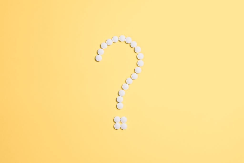 White pills arranged into a question mark shape on a vibrant yellow background.